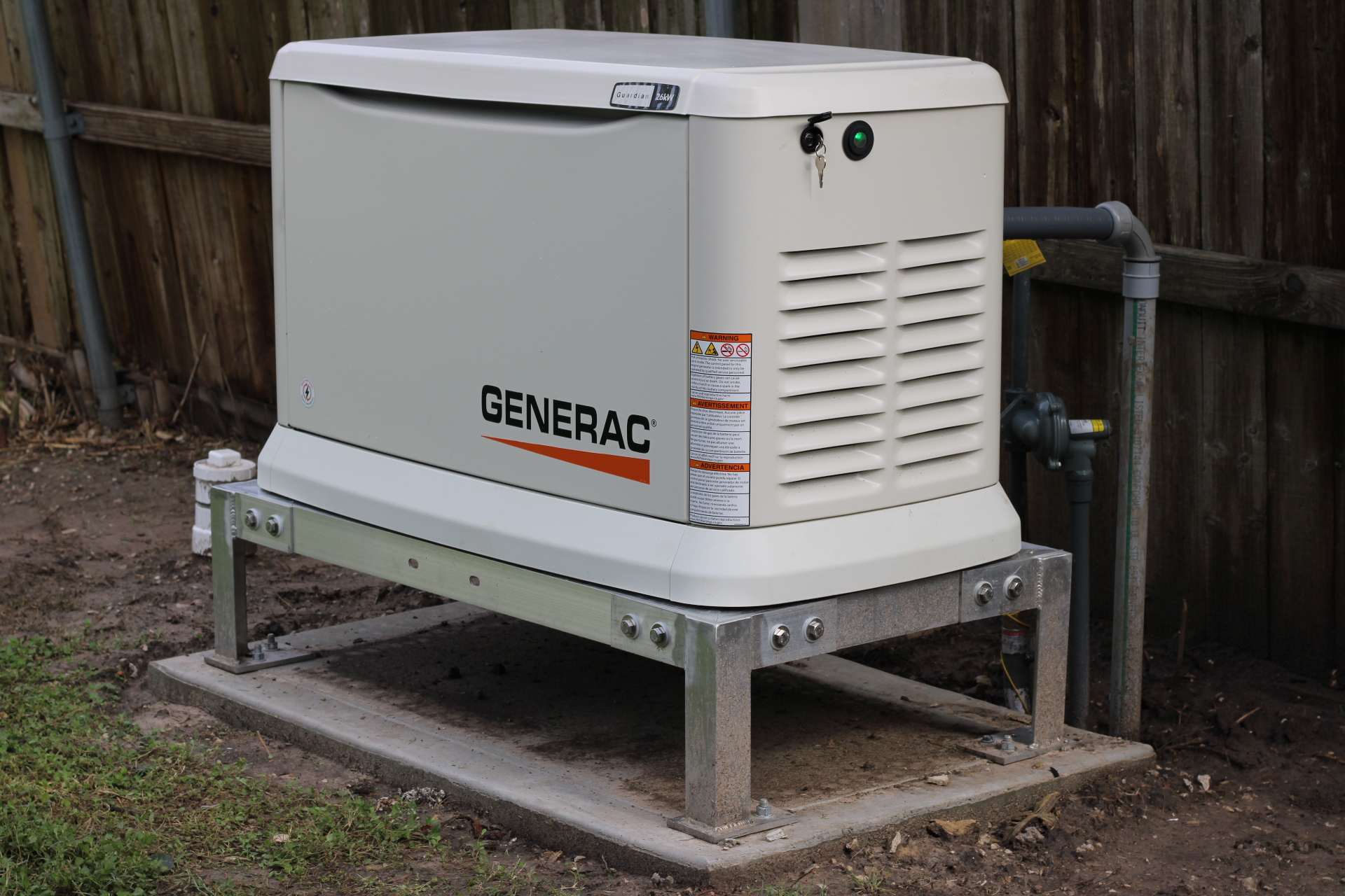 A Generac Guardian 26 kW standby generator set on a galvanised steel platform above its concrete pad, with the gas regulator and piping run in alongside