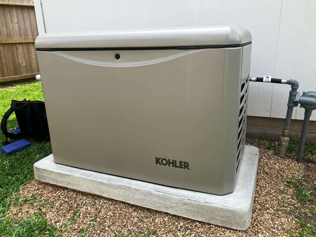 A Kohler standby generator set on its finished concrete pad, with the gas line and shut-off valve run in at the right