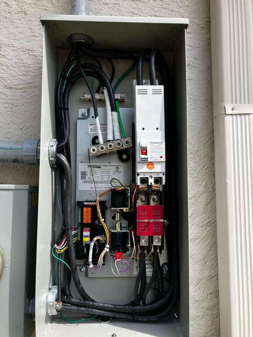 A Generac 200 amp automatic transfer switch mounted beside the meter with its door open, showing the neutral bonding bar, the utility main breaker and the terminations