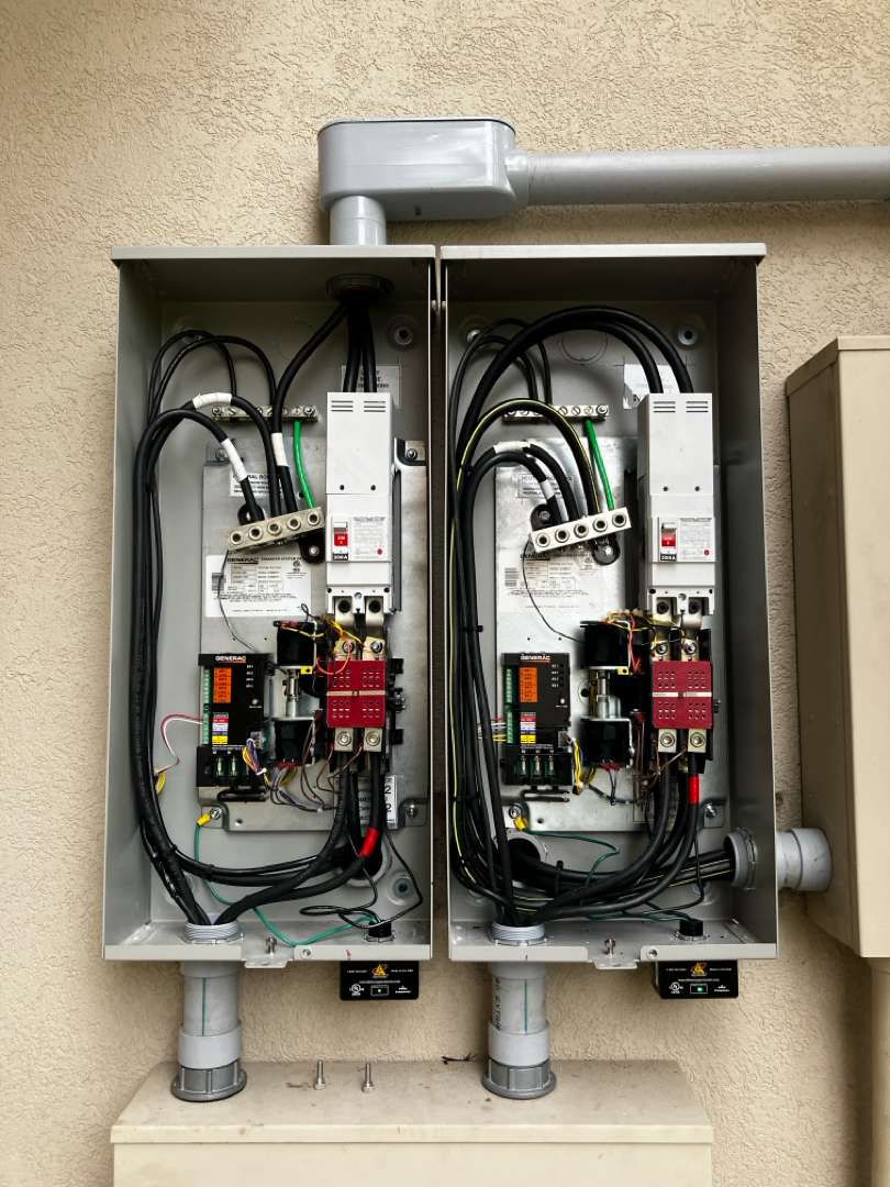 A pair of Generac automatic transfer switches mounted side by side with their doors open, showing the conduit entries, neutral bars and terminations